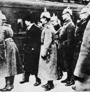 fotografía de León Trotski, con abrigo negro, rodeado de oficiales alemanes en Brest-Litovsk, a fines de 1917.